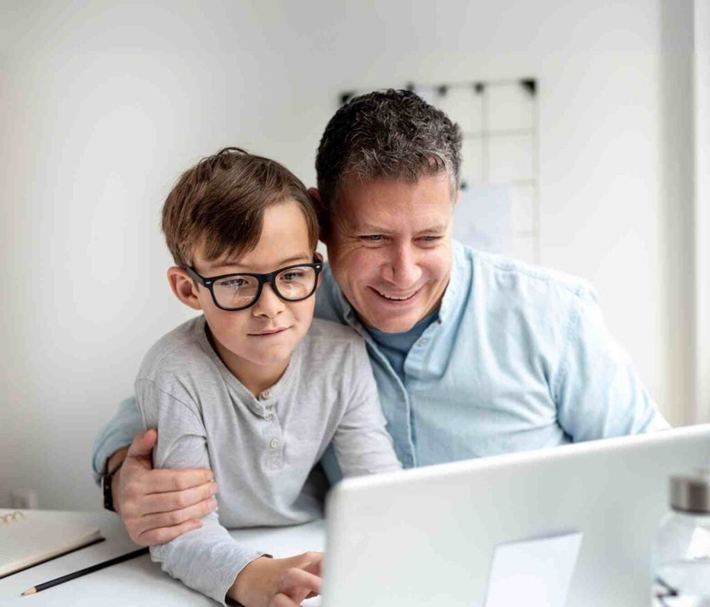 Father and son smiling while using a laptop together, symbolizing learning and connection