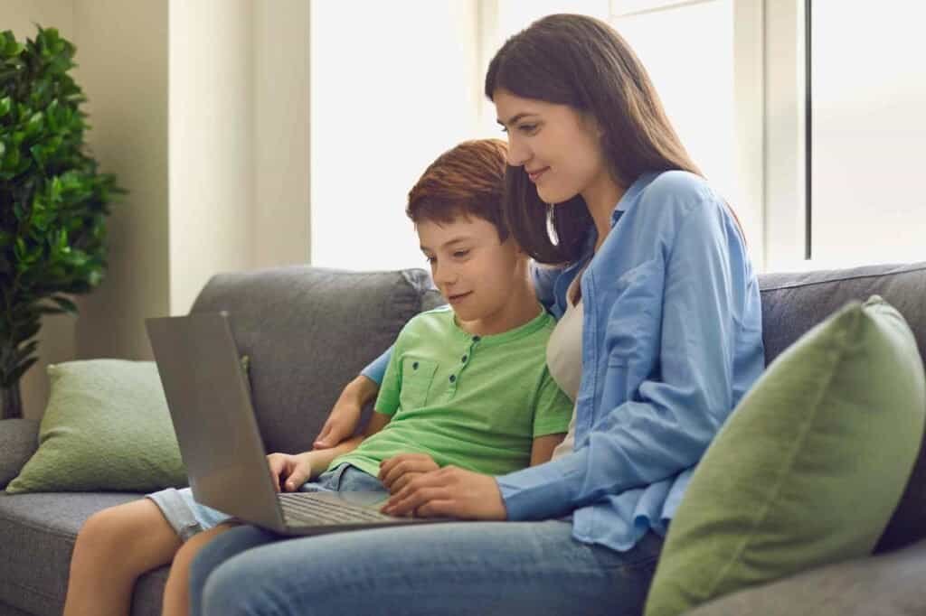 Mother and son sitting on a couch learning together on a laptop at home