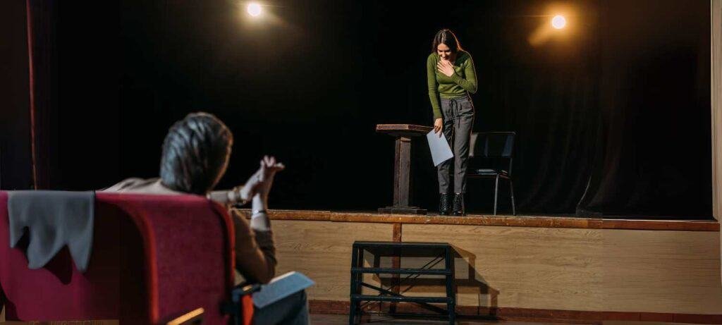 Young performer bowing on stage after audition while coach gives feedback