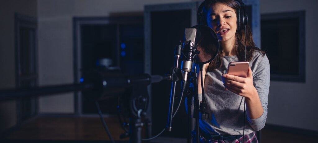 Female professional singer recording vocals in music studio with headphones and microphone