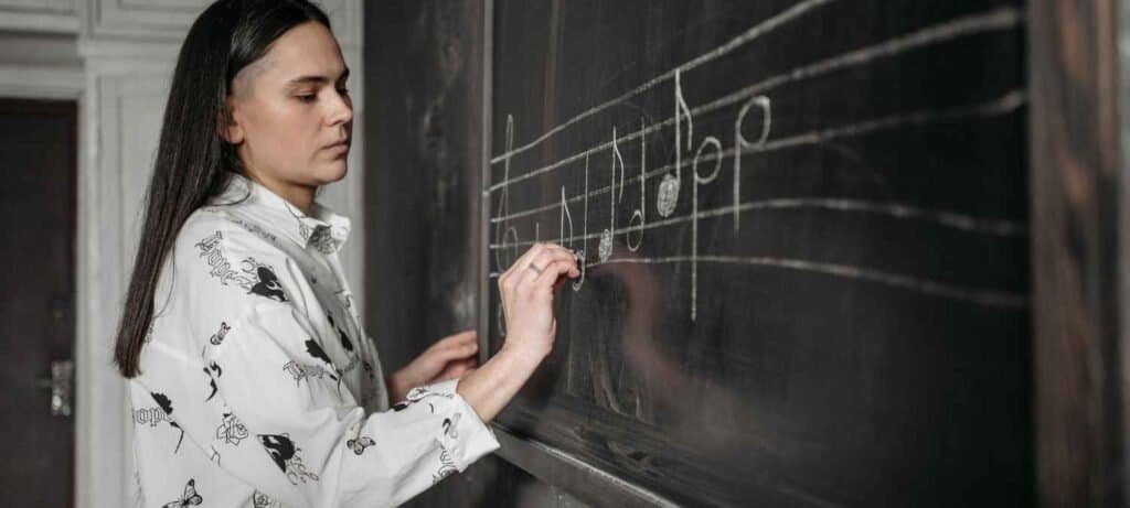 Music teacher drawing notes on chalkboard staff during vocal lesson